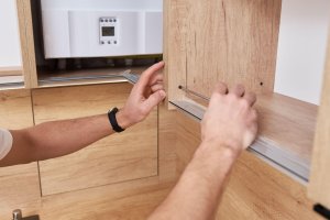 A man installing a cabinet in a kitchen, using a drill and screws