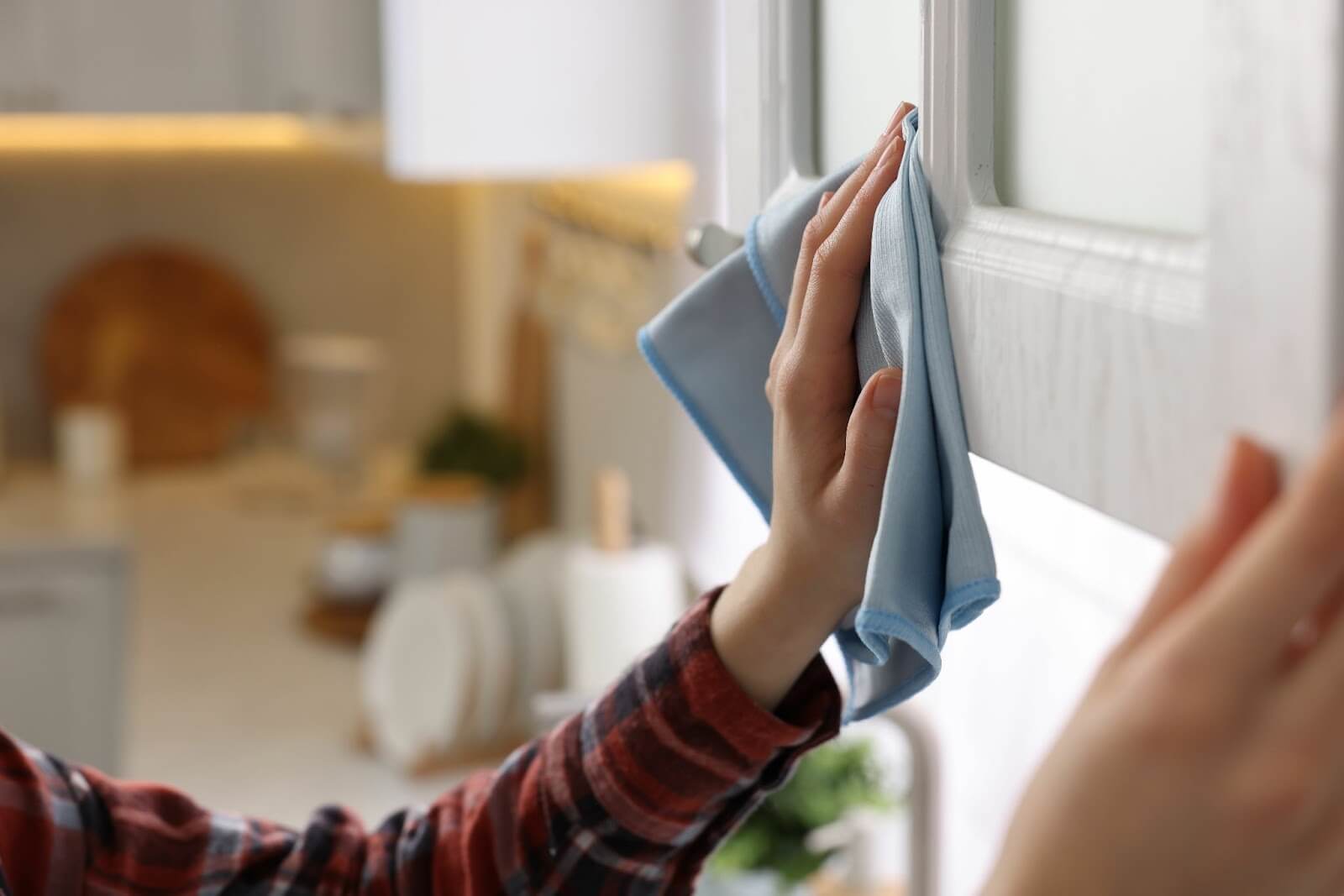 A person cleans a cabinet door with a blue cloth in a kitchen setting.