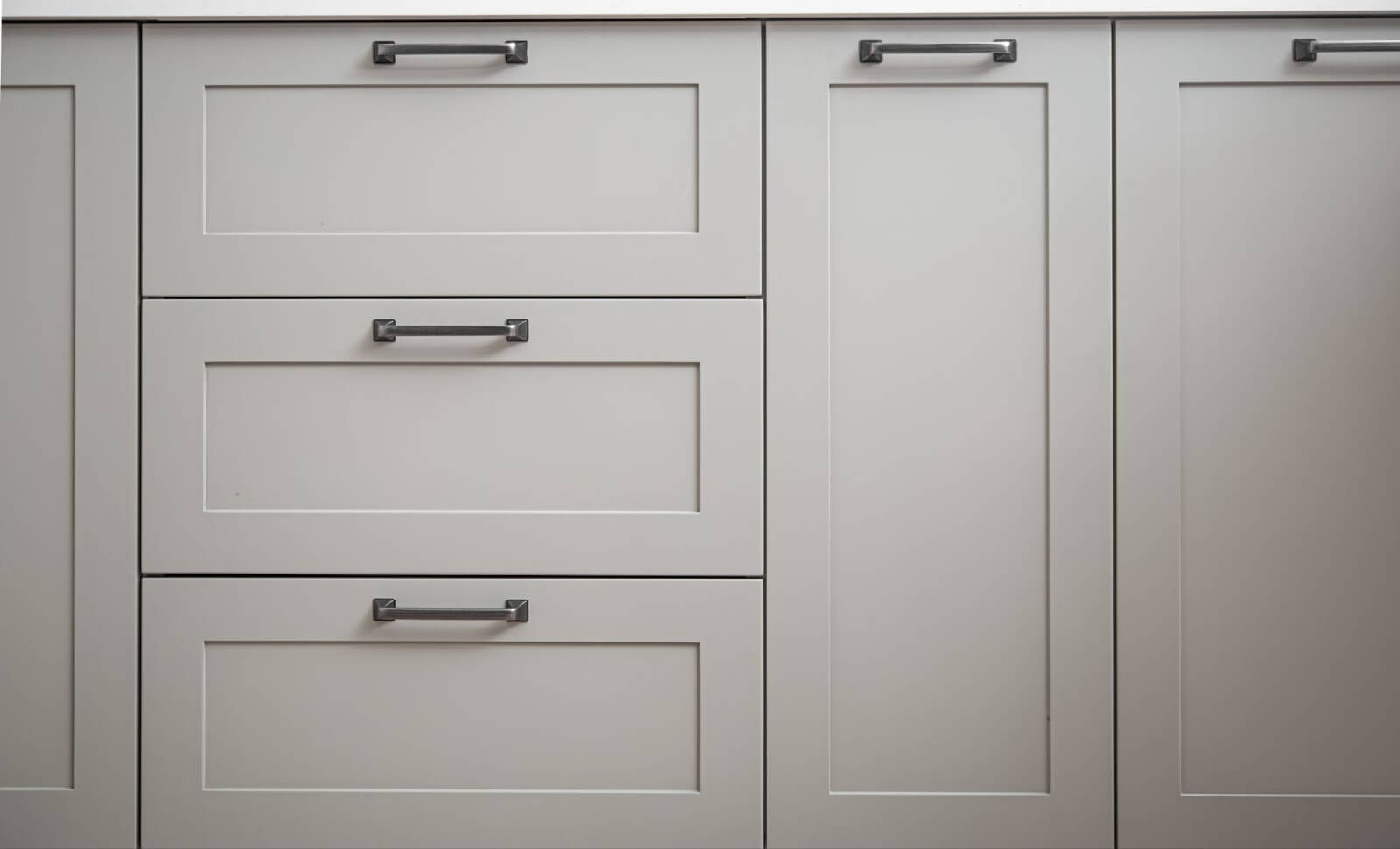 A row of gray kitchen cabinets with black handles.