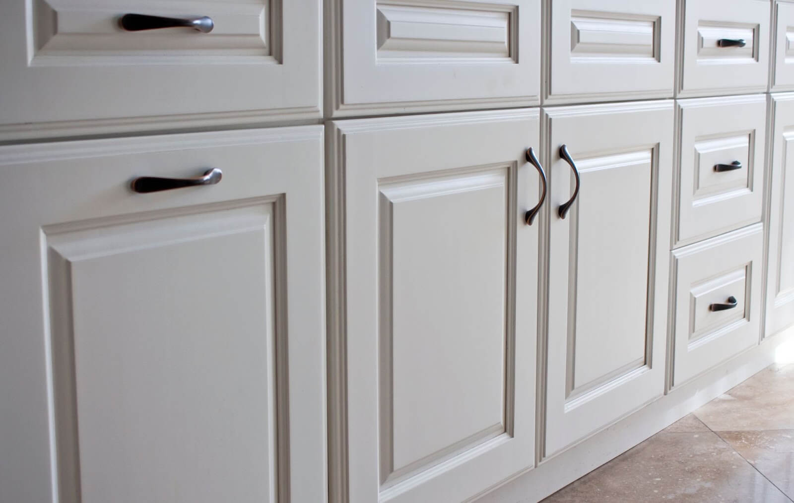 Close-up of white kitchen cabinets with black handles and tiled floor.