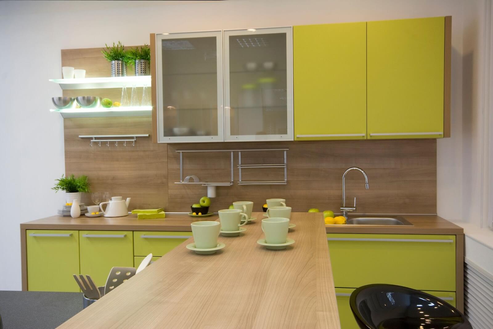 Modern kitchen with yellow cabinets, glassware, green mugs, and potted plants on a wooden countertop.