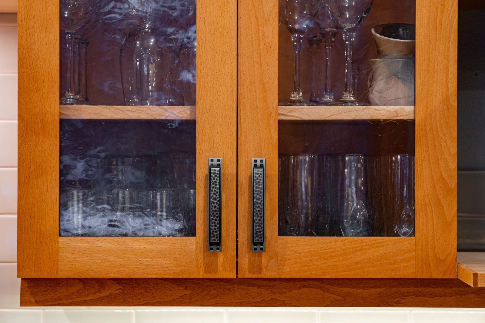 Wooden kitchen cabinet with frosted glass doors and textured black handles, displaying glassware.