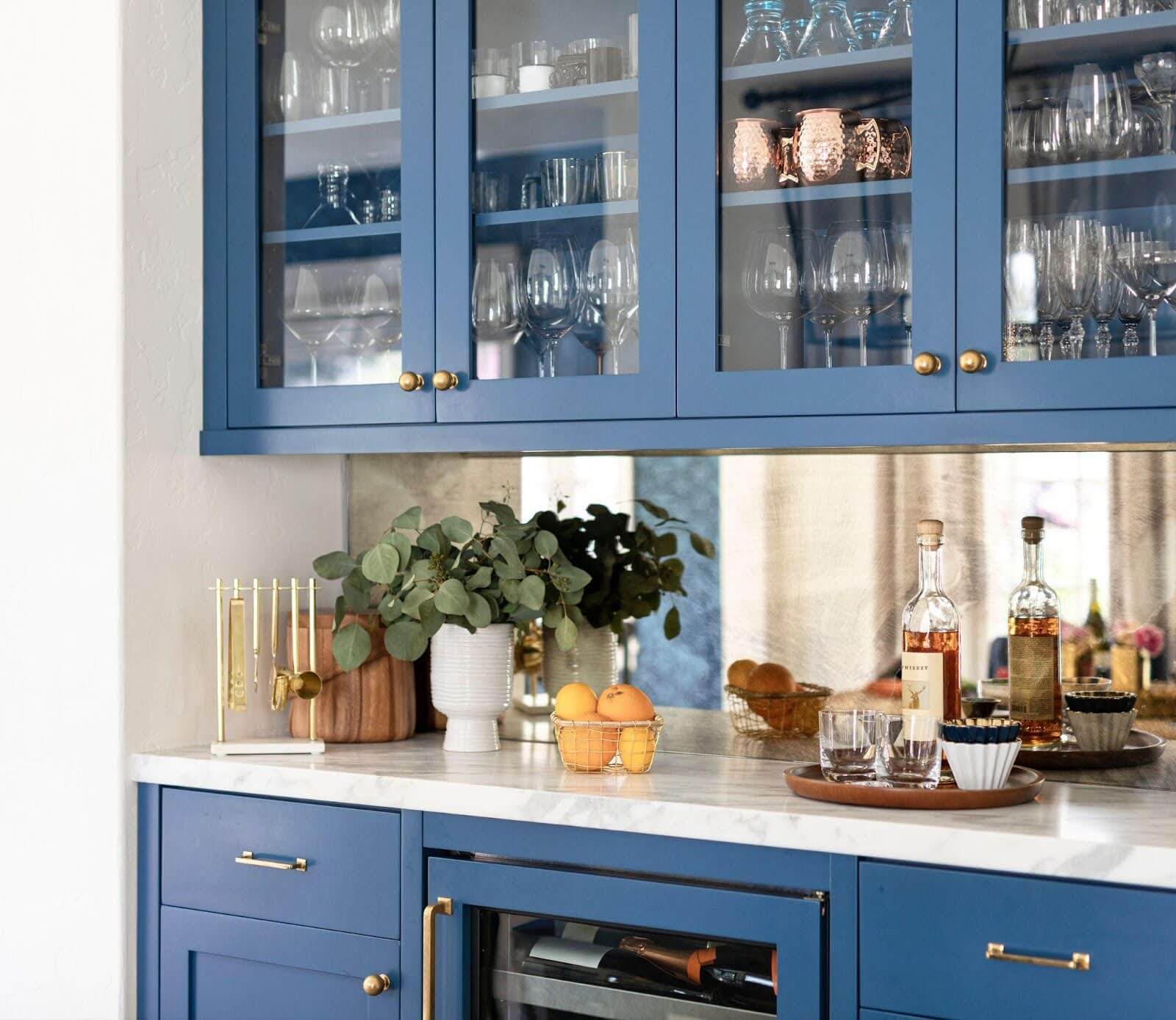 A modern blue kitchen featuring a wine fridge and elegant glass cabinets